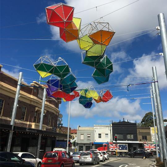 A colourful public artwork is suspended above a street